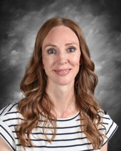 Smiling woman with long, wavy brown hair, wearing a striped shirt, against a gray background.