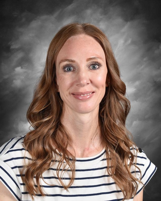Smiling woman with long, wavy brown hair, wearing a striped shirt, against a gray background.